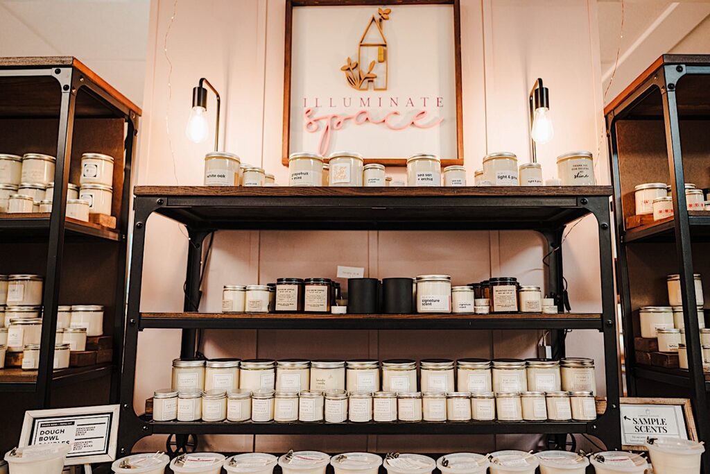 Candles sit on shelves underneath a sign that says illuminate space.  The candles made by Light and Pine Collective are featured in the Wilson Street Mercantile. 