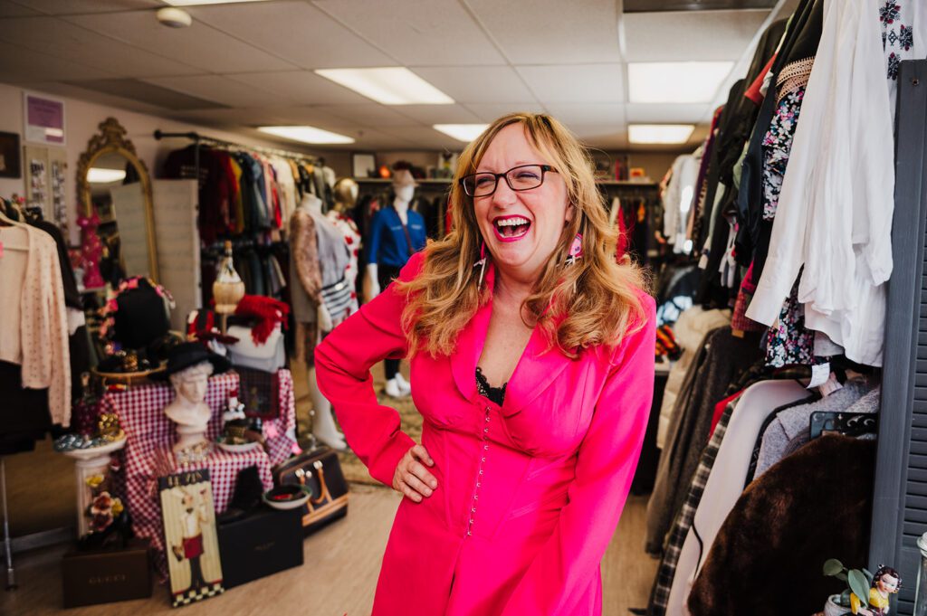 Paula, the owner of the womens consignment shop Paula's in Batavia stands in her shop wearing a hot pink two piece outfit. 