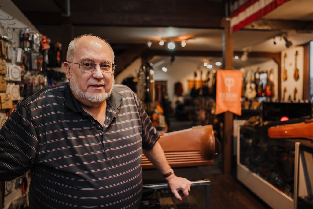 The owner of the Music Exchange, a music shop that sells new and second hand instruments and offers music lessons, stands in his shop smiling at the camera.
